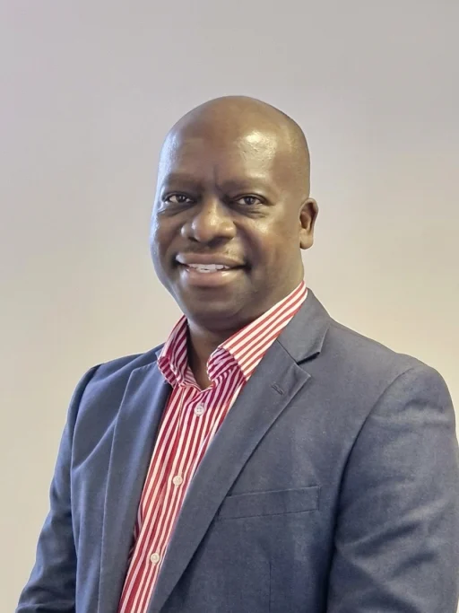 Michael Mbondiah, Managing Director of Virtuous Business Solutions, smiling, in a grey blazer and red striped shirt.